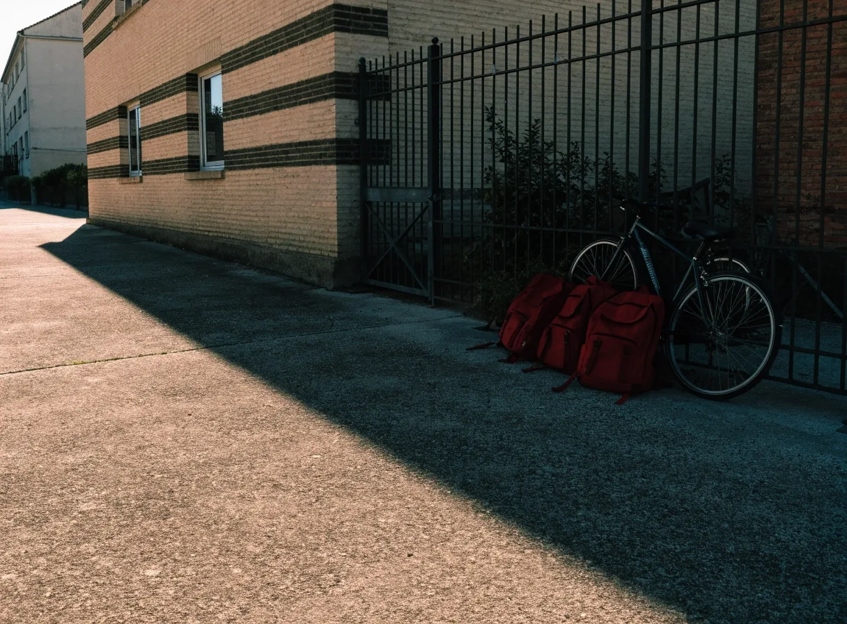 Patio de un colegio de barrio a primera hora con mochilas apoyadas junto a la valla